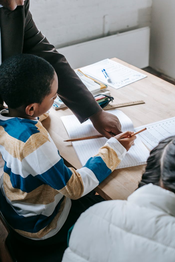 The Art of Drawing Readers In: Your attractive post title goes here Educator helping children with schoolwork at a desk, promoting inclusive learning.