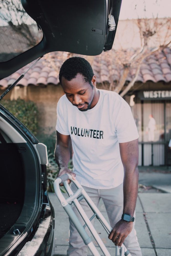 African American man loading a walker into a car trunk while volunteering outdoors.